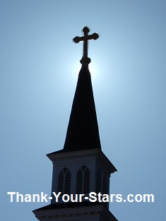 Cross on Church Steeple backlit by the sun with a blue sky background
