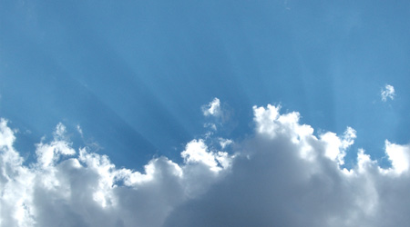 Puffy white clouds and scattered light rays against blue sky